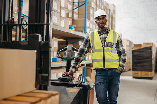 Logistics worker standing next to a forklift in a warehouse