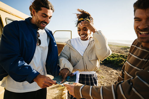 Friends explore coastal road trip with map and smiles near a van by the beach
