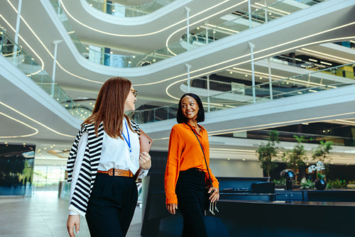 Two female colleagues in the finance industry walking through a large modern corporate building