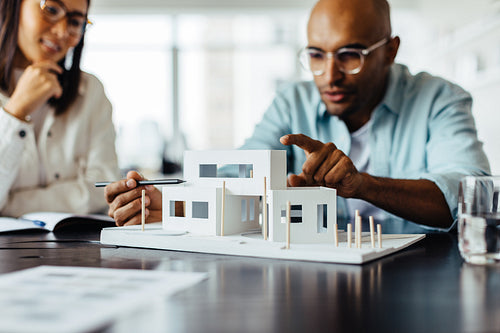 Male architect discussing a 3D house model with his colleague in an office