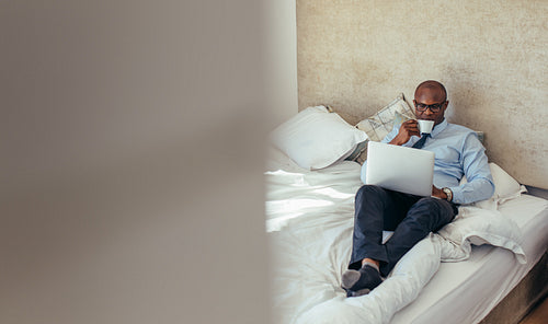 Businessman working on laptop computer lying on bed