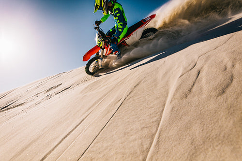 Motocross biker riding on sand dunes in a desert
