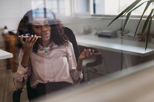 Businesswoman talking over mobile phone on loudspeaker while working at home