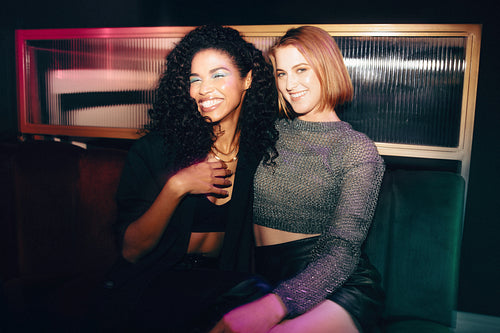 Two women smiling together in a cozy lounge with beautiful lighting