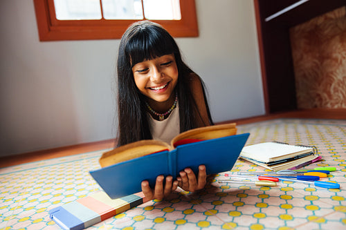Smiling girl reading a book while studying indoors on a colorful floor