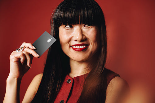 Mature Asian woman embraces the rise of exclusive banking as she smiles with a  black credit card in her hand