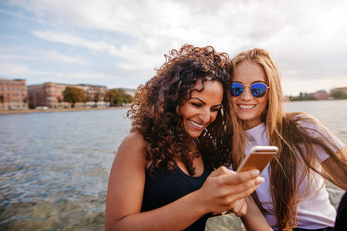 Female friends using smart phone by the lake