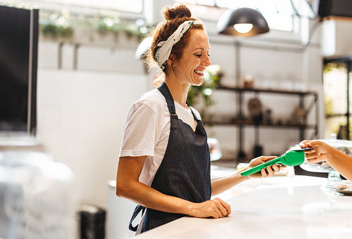 Happy barista getting a credit card payment from a customer