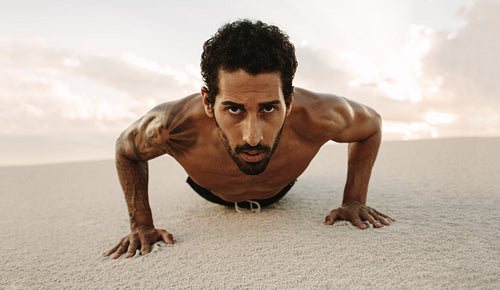 Male athlete doing push ups on desert sand