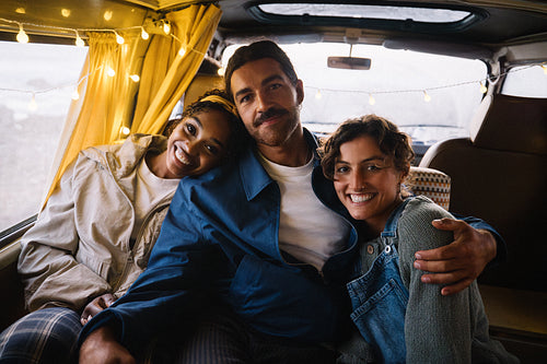 Three friends on a cozy road trip inside a van with string lights