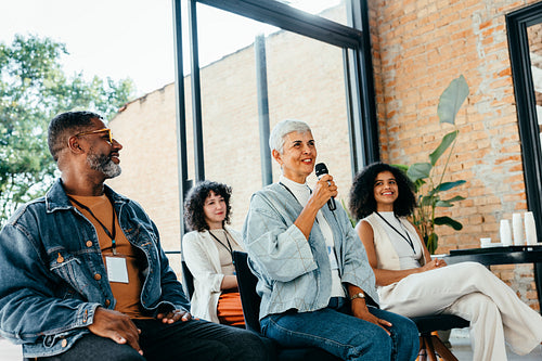 Female speaker presenting with microphone to colleagues during business meeting