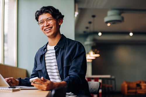 Smiling young man using a laptop and smartphone in a casual setting
