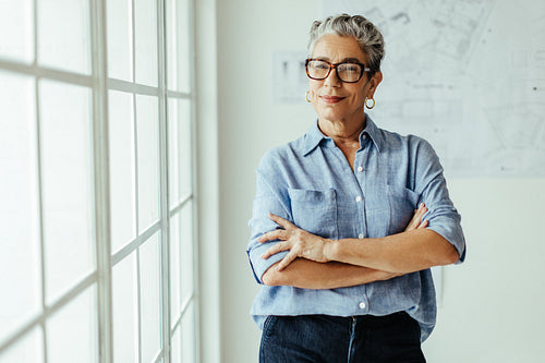 Successful and empowered female architect standing in her office with crossed arms