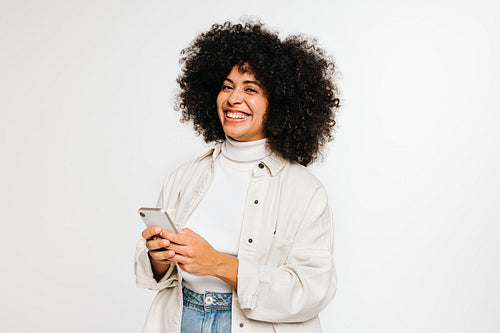 Happy young woman smiling at the camera while holding a smartphone