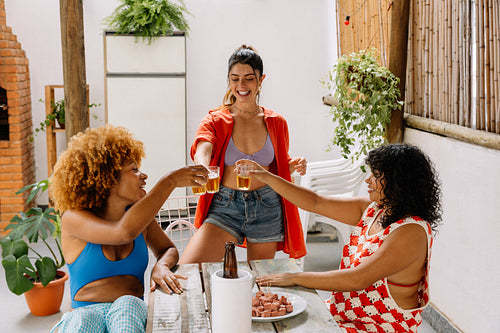 Three women toasting drinks together in a lively Brazilian outdoor setting