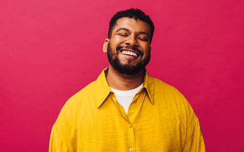 Happy young man smiling cheerfully with his eyes closed