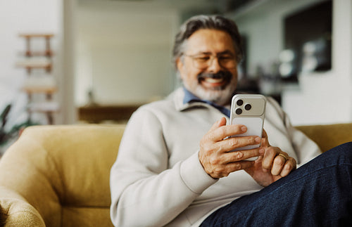 Senior man uses a smartphone while relaxing at home