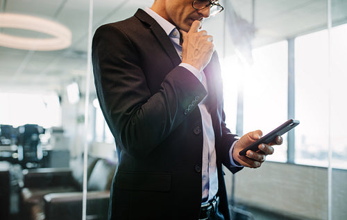 Businessman using mobile phone in office and thinking