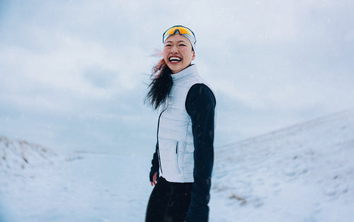 Smiling woman runner poses in winter snow with sportswear outdoors