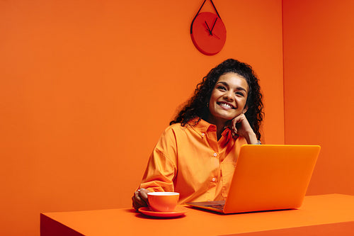 Happy woman working on laptop in vibrant monochromatic orange setting with copy space