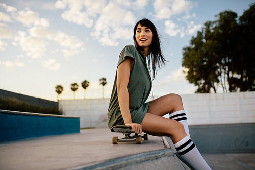 Beautiful skateboarder sitting at skate park