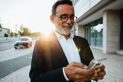 Professional senior man checks his phone outdoors during a sunny afternoon