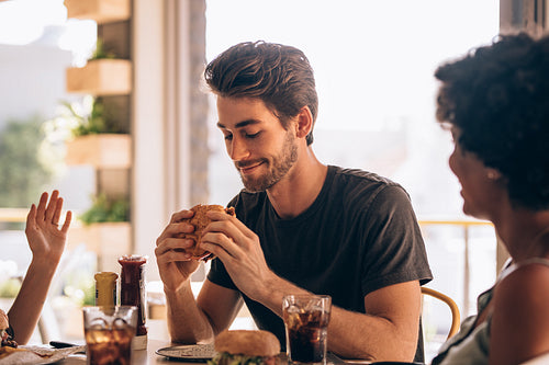 Man eating burger with friends at restaurant