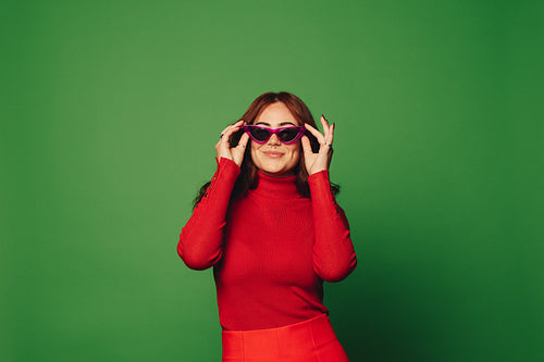 Smiling woman wearing stylish sunglasses and trendy sweater on vibrant green background