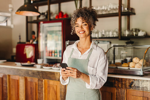 Female cafe owner holding a smartphone in her shop