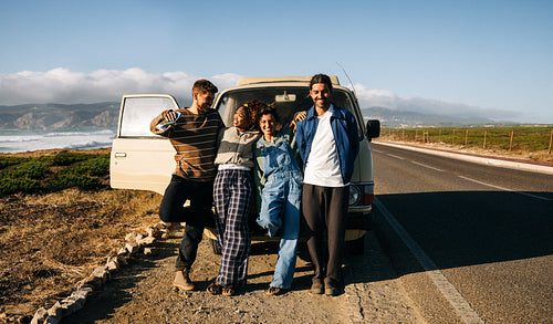 Friends on road trip with van by coastal highway at sunset