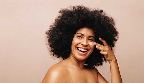 Cheerful woman with Afro hair applying moisturizing cream on her face