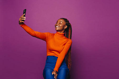 Smiling african woman taking a selfie with smartphone on a vibrant purple background