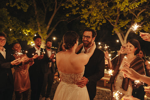 Romantic newlyweds celebrate with sparklers surrounded by friends in a nighttime garden