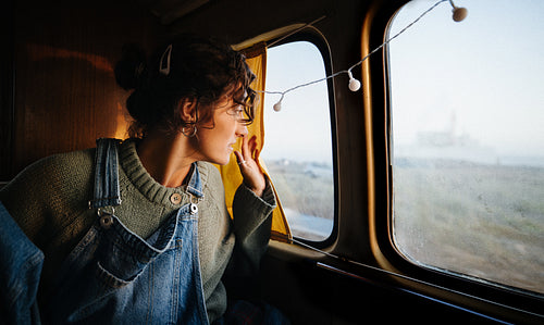 A woman looks out a camper window enjoying a calm morning