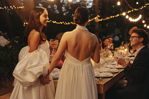 Two brides celebrating hand in hand at outdoor LGBTQ wedding reception