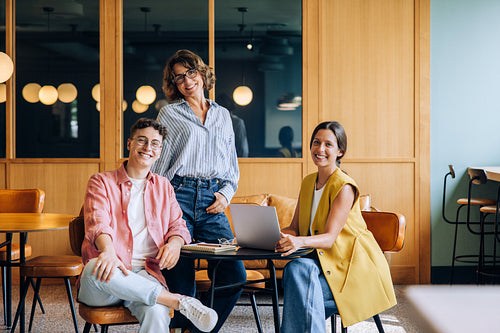 Three colleagues in a casual setting discussing ideas and working on a laptop