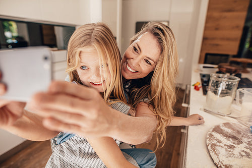 Beautiful woman and her cute daughter taking selfie in kitchen