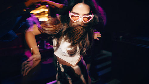 Woman dancing with heart sunglasses under party lighting at a lively nightclub
