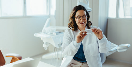 Female dentist smiling while demonstrating dental aligner in clinic
