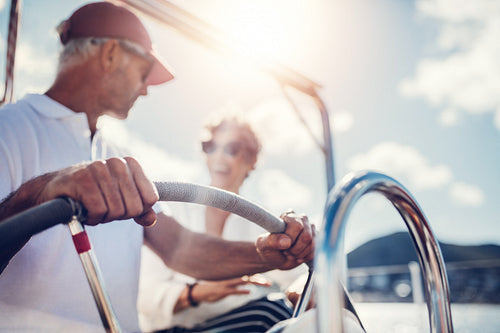 Senior man steering a boat with his wife in background