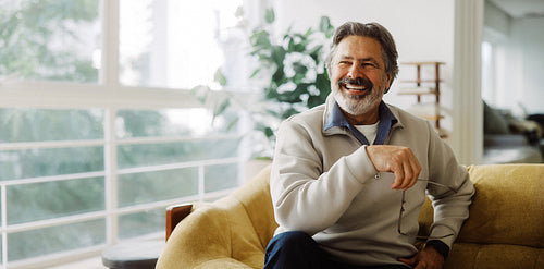 Laughing senior man sits in an armchair at home