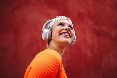 Happy woman enjoys music streaming with headphones  against bright red wall