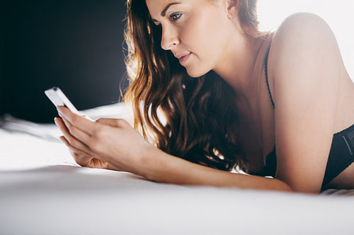 Beautiful young woman on bed texting with her cell phone