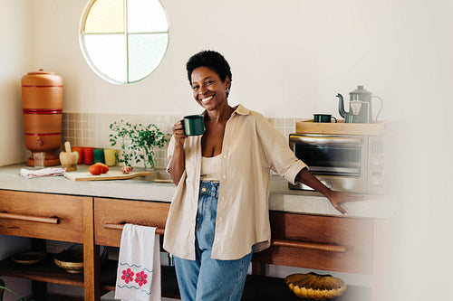Happy brazilian woman smiling and holding a cup of coffee in the kitchen