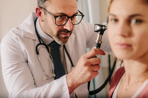 ENT doctor checking ear with otoscope of woman patient