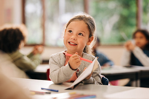 Excited little girl learns to draw with a colour pencil in an art class