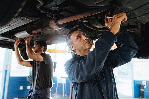Mechanics fixing car exhaust system in garage 