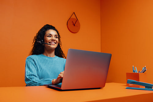 Happy support agent working on laptop in colourful office with bold colour blocking