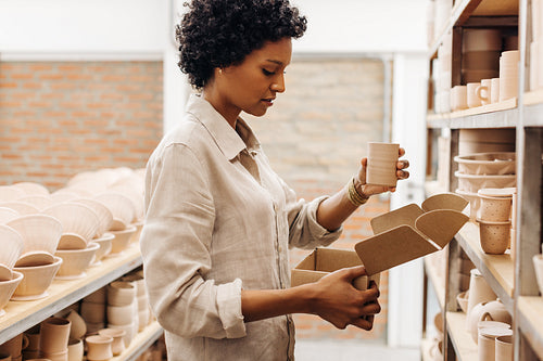 Female ceramic shop owner packaging one of her earthenware products into a box