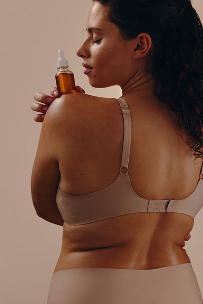 Woman with serum bottle on shoulder applying skincare oil